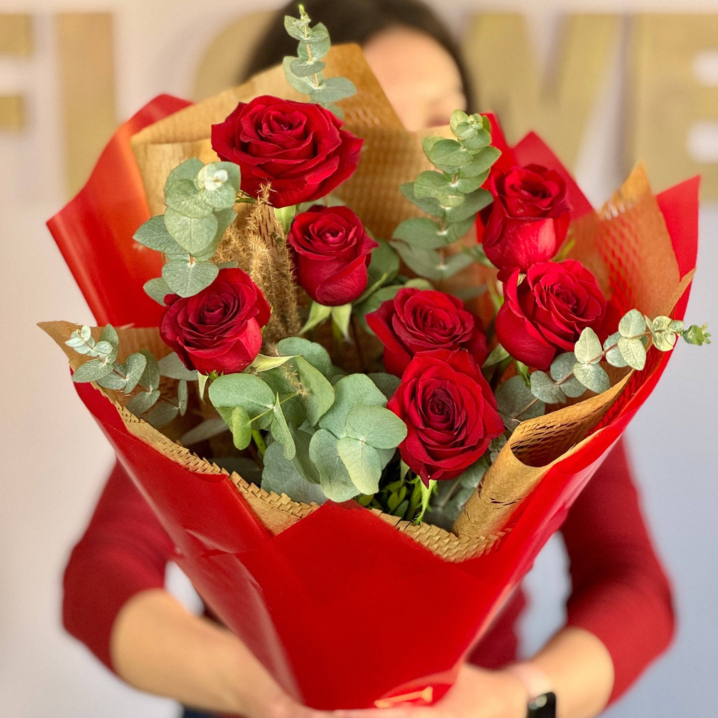 Buchet de trandafiri roșii și eucalipt, ambalat elegant în hârtie roșie, ideal pentru aniversări, cereri în căsătorie sau surprize romantice.