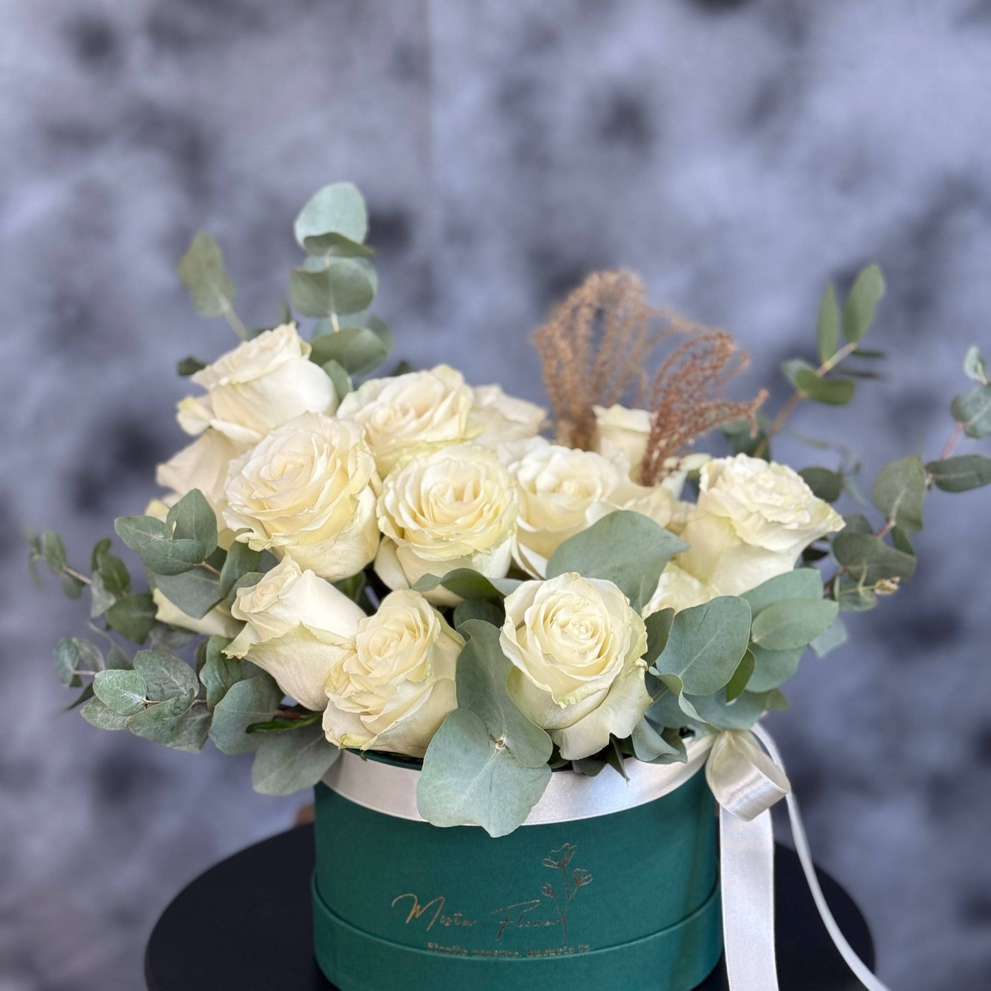 Aranjament cu trandafiri albi și eucalipt în cutie verde catifelată, cadou elegant pentru ocazii speciale în Florești și Cluj. Design floral rafinat cu flori naturale.