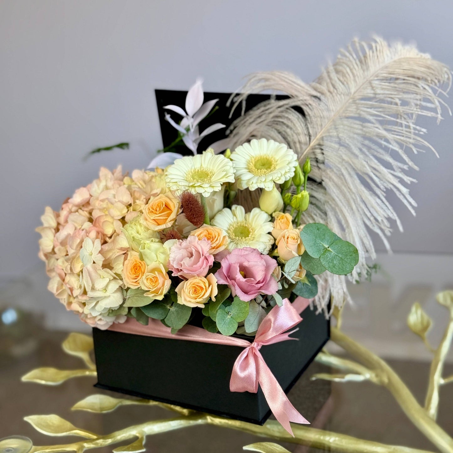 Aranjament floral elegant în cutie neagră, cu hortensii, trandafiri, gerbera, lisianthus și pampas, decorat cu o fundă roz satinată.